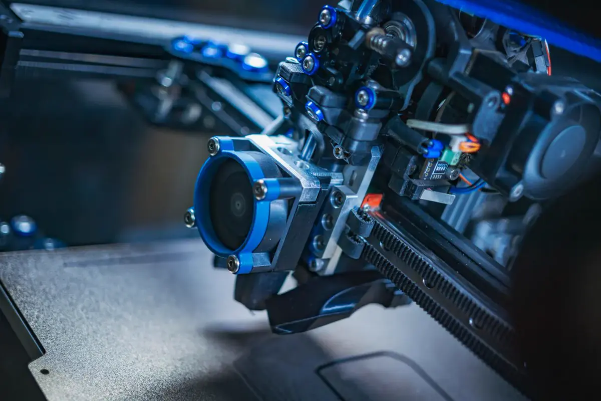 Gros plan sur la tête d’impression bleue et noire d’une imprimante 3D, au-dessus de son plateau